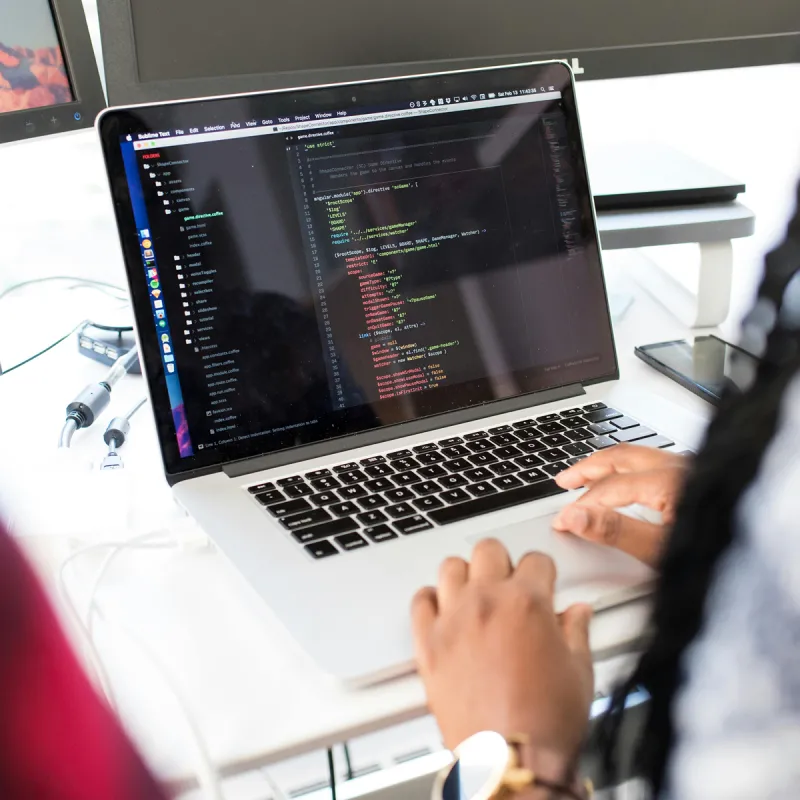 Woman sat at a desk with a Macbook where she is writing code to develop a game Woman sat at a desk with a Macbook where she is writing code to develop a game