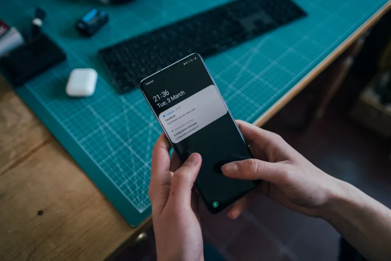 person sat at work desk with two hands holding a black iphone displaying new notifications  person sat at work desk with two hands holding a black iphone displaying new notifications