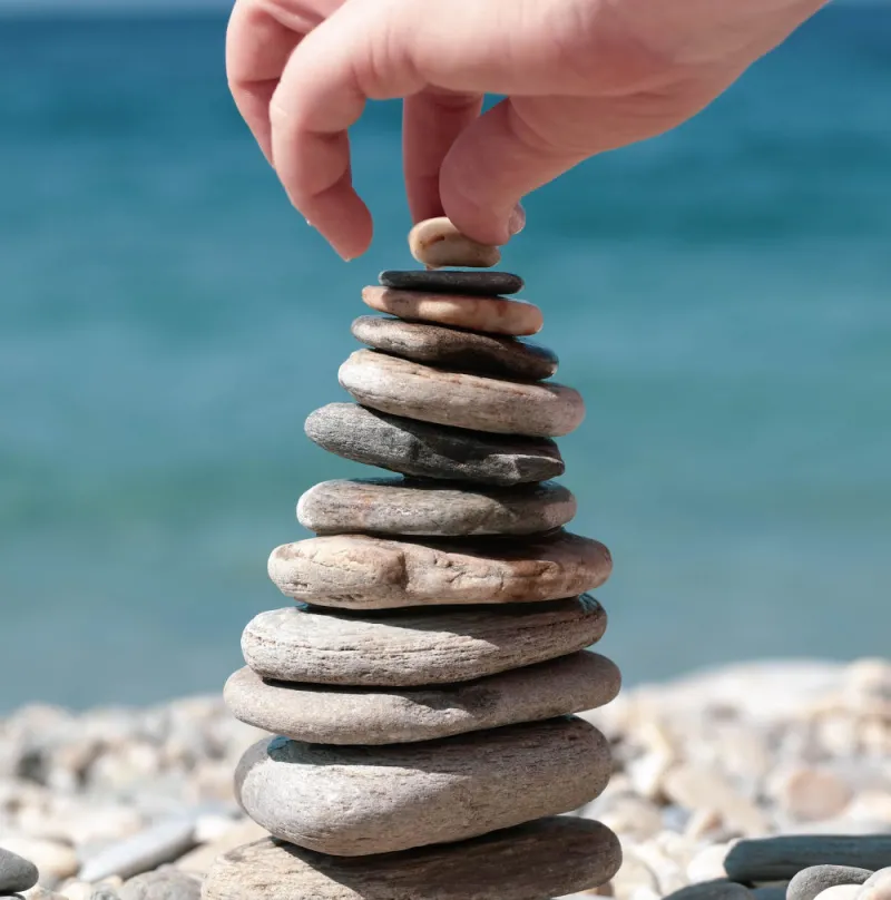 a-han-balancing-grey-pebbles-on-top-of-each-other-in-front-of-a-blue-sea