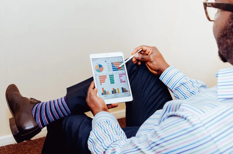 Person sitting on a chair, holding an ipad with analytics information Person sitting on a chair, holding an ipad with analytics information