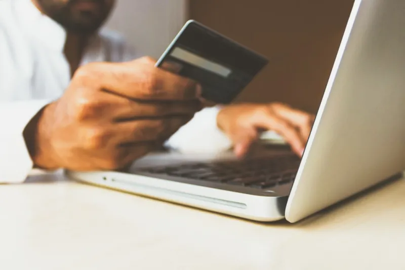 Image of a man holding a card and using a laptop Image of a man holding a card and using a laptop