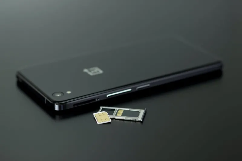 black mobile phone next to a sim card on a black background black mobile phone next to a sim card on a black background