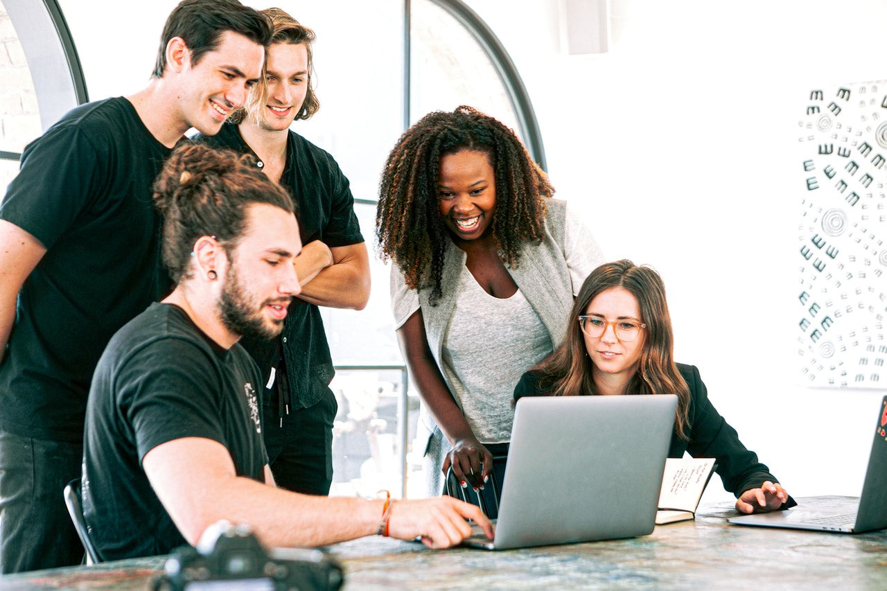 an office team dressed casually sat round a laptop smiling